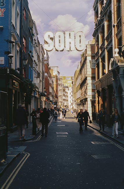 View of Carnaby Street in daylight, featuring a pedestrian street lined with narrow, multi-story buildings that have a mix of colorful facades and traditional brickwork. The street is bustling with pe